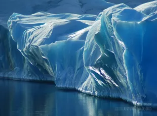 Sun-reflecting blue front of a larger iceberg