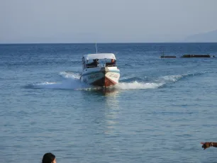 DSCN1023.JPG: A small motorboat cuts through calm blue waters toward the shore on a clear day, leaving a V-shaped wake behind.