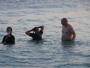 DSCN1049.JPG: Three people stand waist-deep in calm ocean water at dusk, chatting and relaxing as gentle waves lap around them.