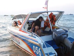 DSCN1069.JPG: A small speedboat numbered 056 pulled up on the shore as a passenger climbs aboard, life jackets secured inside and the sea stretching into the distance.