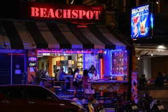 DSC_3547: Beachfront bar "BEACHSPOT" glowing with neon lights as patrons chat and relax at outdoor tables on a lively night.