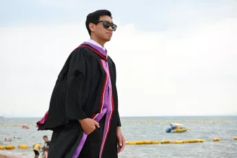 DSC_3817: A proud graduate in cap and gown stands by the seaside, looking toward the future with confidence and a smile.