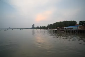 DSC_2352: Calm waterfront at dusk with gentle ripples reflecting the soft pastel sky and low-lying buildings along the shore.