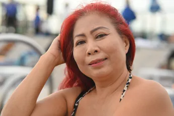 DSC_2728: Smiling woman with red hair relaxing outdoors in a patterned swimsuit, looking confidently at the camera.