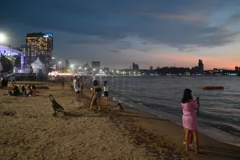 DSC_6246: Evening settles over a lively city beach as people stroll the shoreline, take photos, and enjoy the waterfront lights.