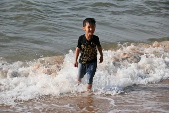 DSC_6824: A young boy laughing as waves splash around his legs while he plays at the shoreline.
