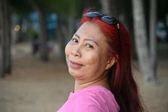 DSC_7245: Smiling woman with vibrant red hair and sunglasses perched on her head, turning to enjoy a moment at the beach.