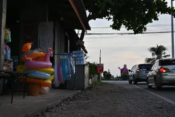 DSC_7554: A roadside stall displays colorful inflatable swim rings and pool toys as cars pass by on a quiet street at dusk.