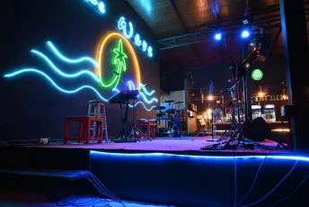 DSC_7624: Neon-lit stage at a beach-themed bar, ready for live music under a glowing palm and rolling waves.