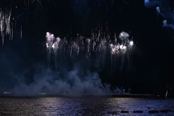 DSC_6210: Silver fireworks cascade over a moonlit sea, their sparkles mirrored on the water below.
