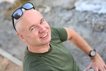 DSC_6352: Smiling man in a green t-shirt looks up at the camera with sunglasses resting on his head and a watch on his wrist.