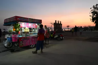 DSC_7780: A colorful street food cart glows at dusk as vendors and a few evening strollers enjoy a seaside sunset.
