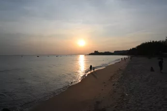 DSC_7748: Golden sun dips toward the horizon as a lone figure walks the peaceful shoreline, leaving footprints in the wet sand.