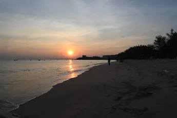 DSC_7758: A tranquil sunset casts golden reflections across the calm sea as a lone figure walks along the quiet, sandy shoreline.