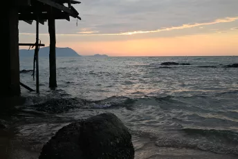 DSC_8984: Sunset light washes the sea as weathered pilings and rocky shore stand quiet against the evening tide.