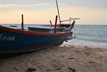 DSC_8980: A weathered fishing boat rests on the sandy shore as the sun sets over a calm sea.