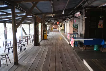 DSCF1089: Quiet wooden riverside walkway lined with small stalls and empty stools, bathed in soft daylight.