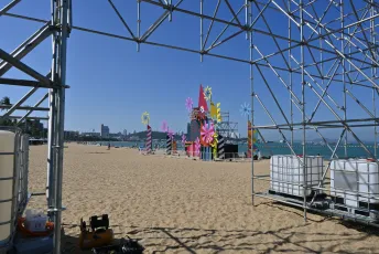 DFC_4043: Bright, sunny day on the beach as colorful festival sculptures rise against the blue sky and sea.