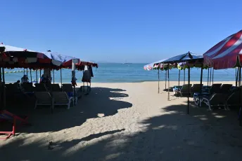 DFC_4017: Shaded loungers and colorful umbrellas line a quiet sandy beach, framing a calm blue sea under a clear sky.