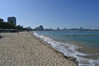 DFC_4020: Sunny morning stroll along a wide sandy beach with gentle waves and a distant city skyline.