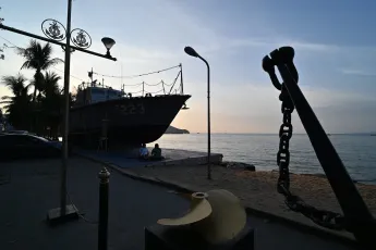 DZ6_2346: Sunset at the waterfront, a moored patrol boat, a large anchor and calm sea silhouette against the evening sky.