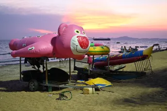 DFC_5152: Sunset over Pattaya beach - colorful inflatable rides resting on the sand as the evening sky glows.