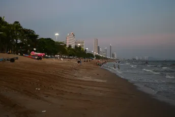 DFC_5141: Twilight on Pattaya Beach, evening lights begin to glow as locals and visitors stroll the shoreline with the city skyline rising in the distance.